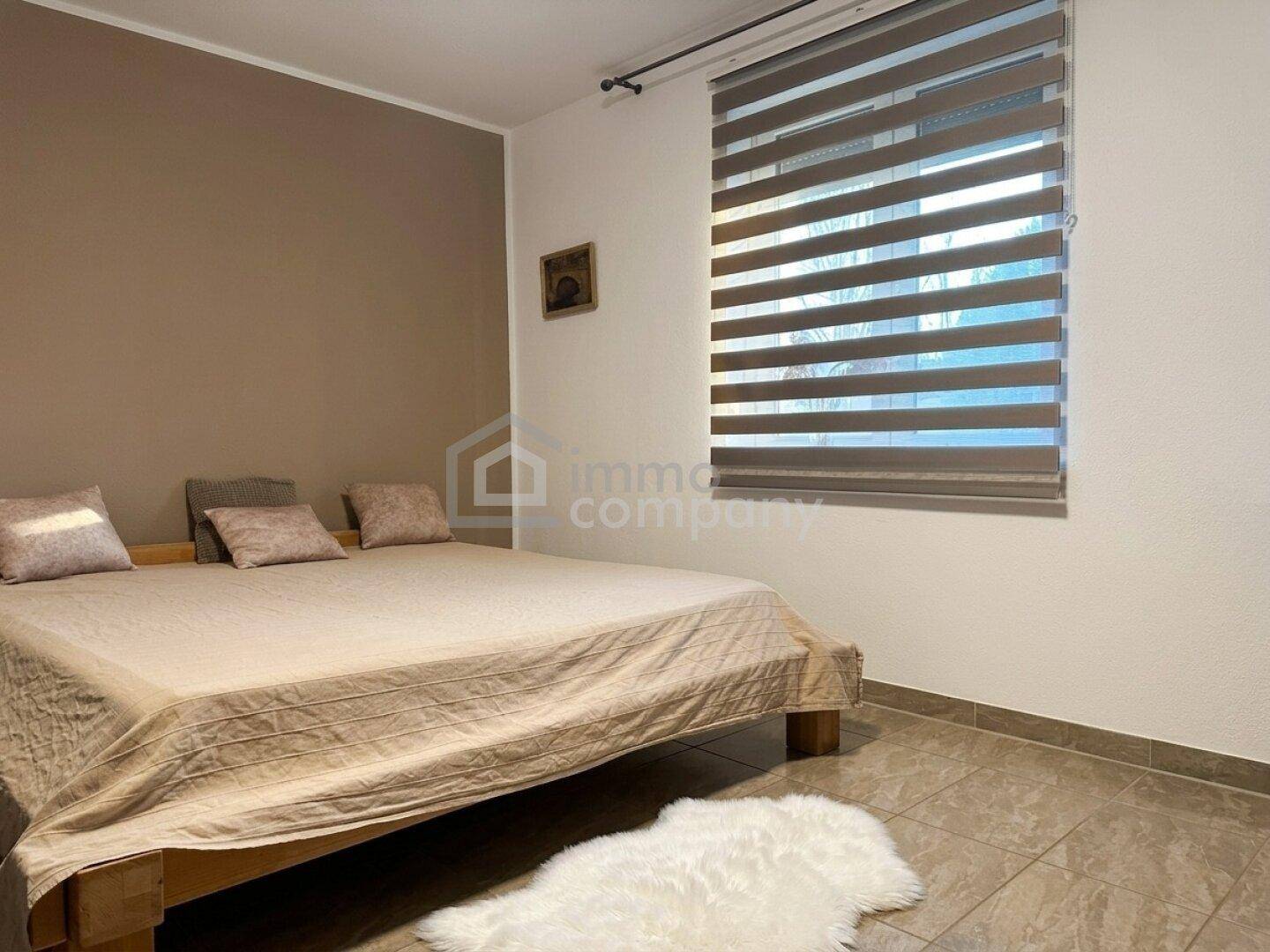 Schlafzimmer mit Doppelbett, Fliesenboden und einem Fenster mit Jalousien für Privatsphäre.