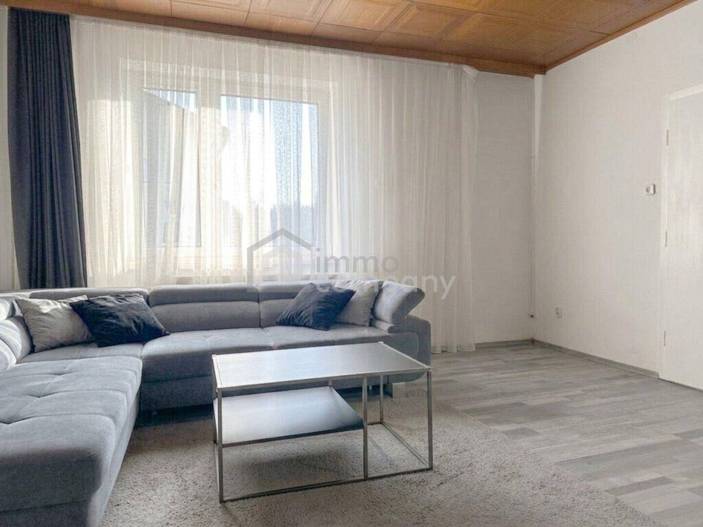 Helles Wohnzimmer mit großem Ecksofa, Laminatboden und viel Tageslicht durch das Fenster.