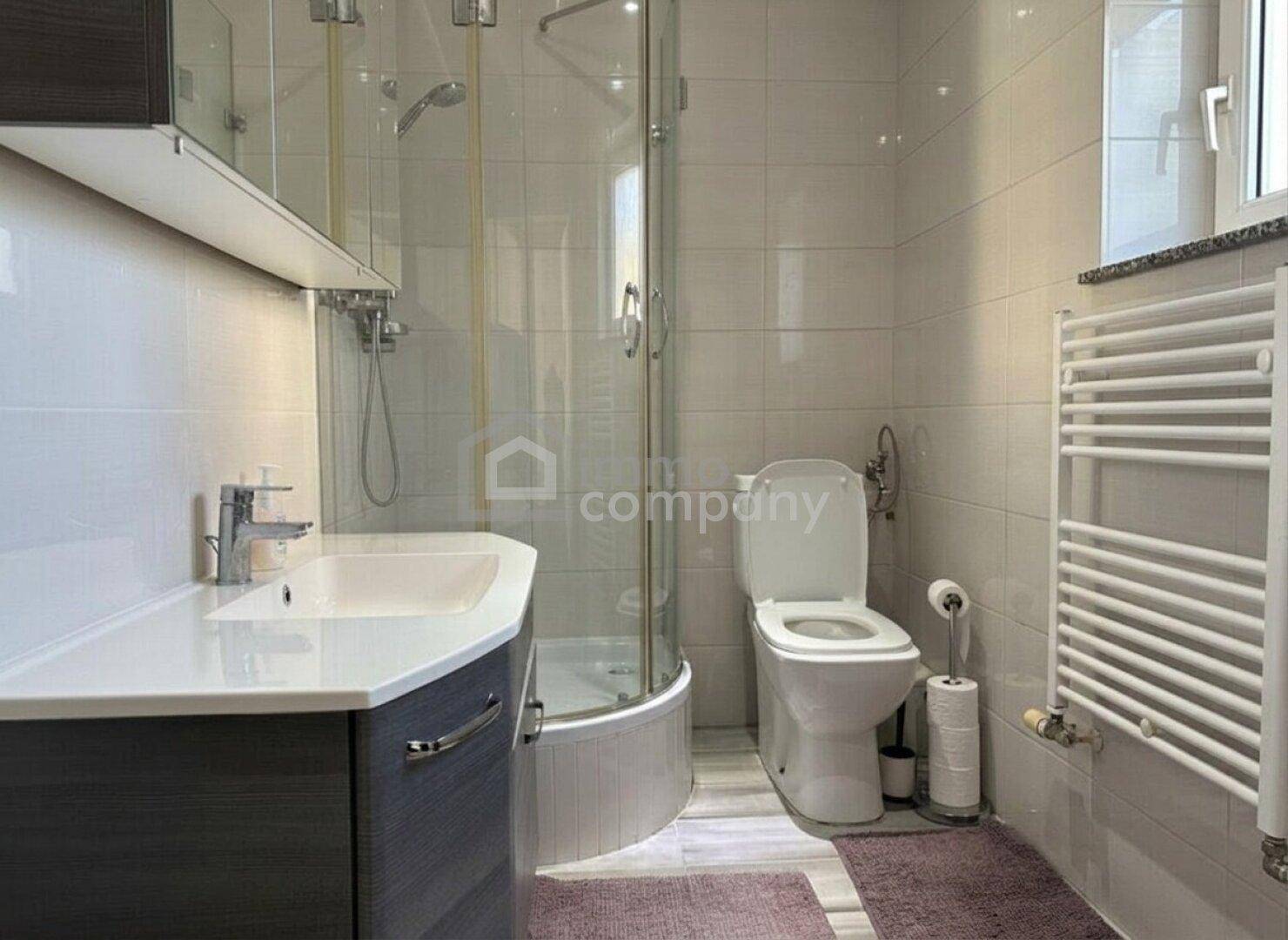 Modernes Badezimmer mit Duschkabine, WC, Einzelwaschbecken und beheiztem Handtuchhalter.