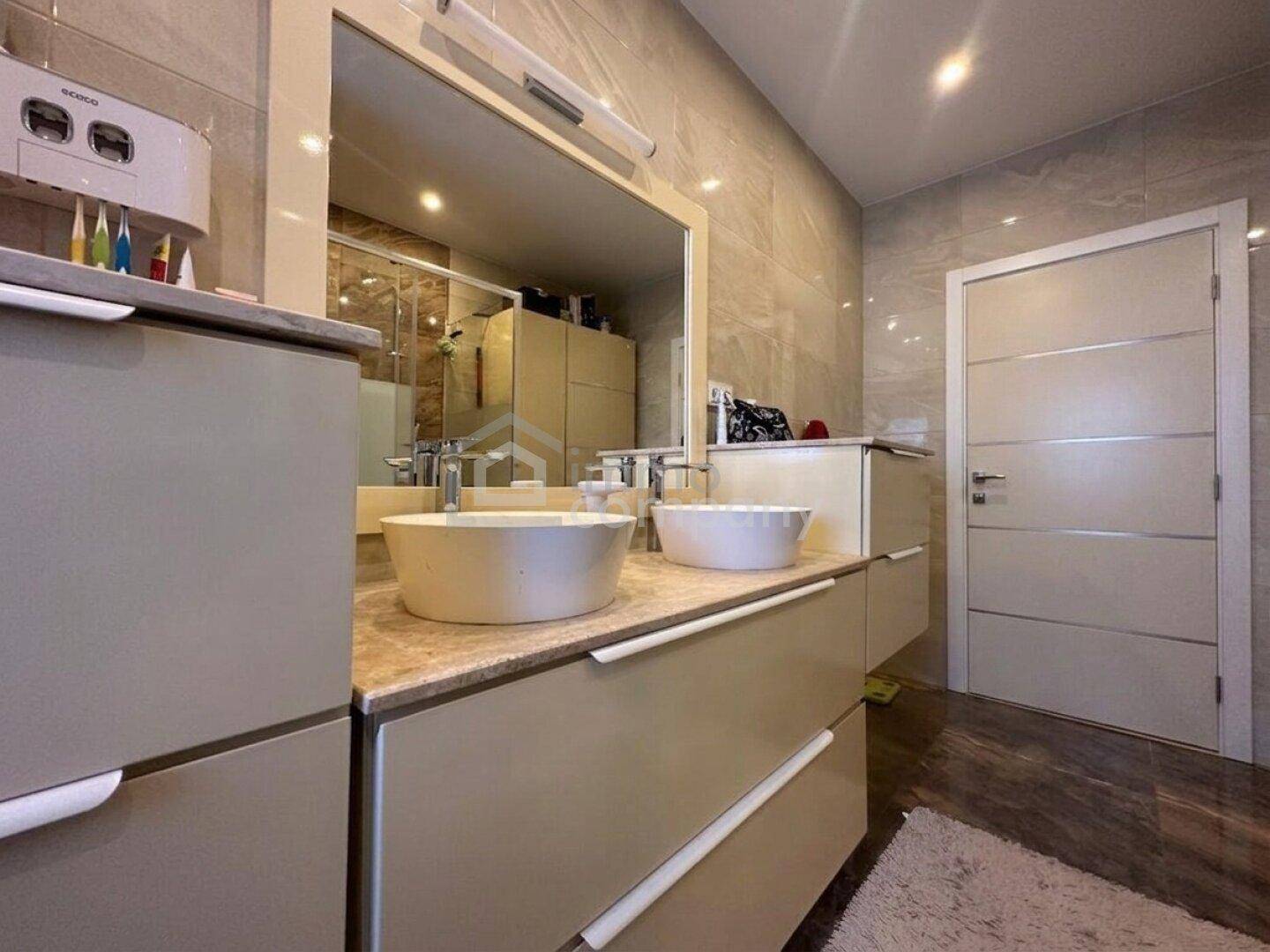Modernes Badezimmer mit Doppelwaschbecken, großem Spiegel und eleganten Fliesen.