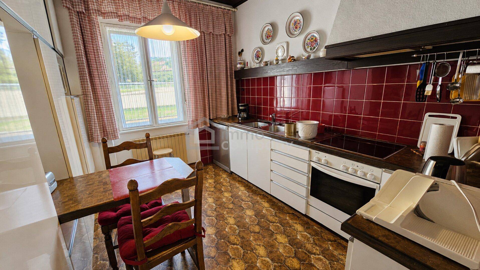 Traditionelle Küche mit roten Fliesen, Holztisch und Blick ins Grüne.