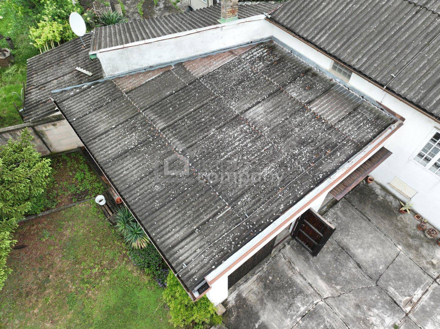 Detailaufnahme eines dunklen Wellblechdaches über einem Garagenbereich mit angrenzender Grünfläche.