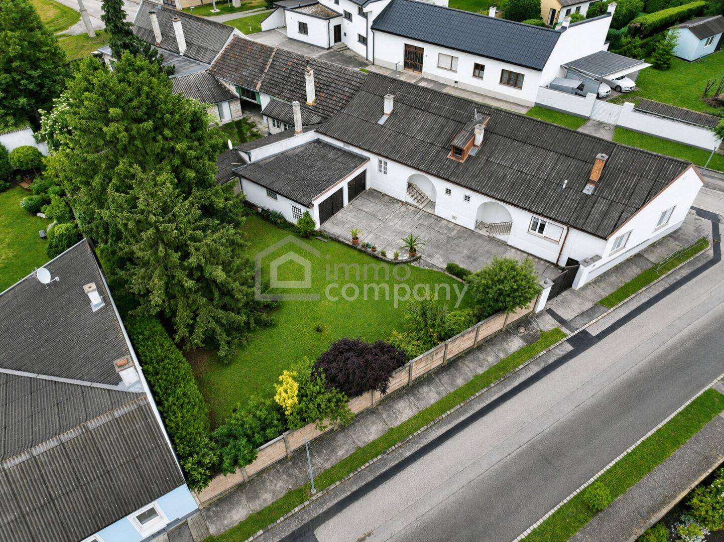 Luftaufnahme eines Anwesens mit weißem Gebäude, großem gepflasterten Hof und gepflegtem Gartenbereich.