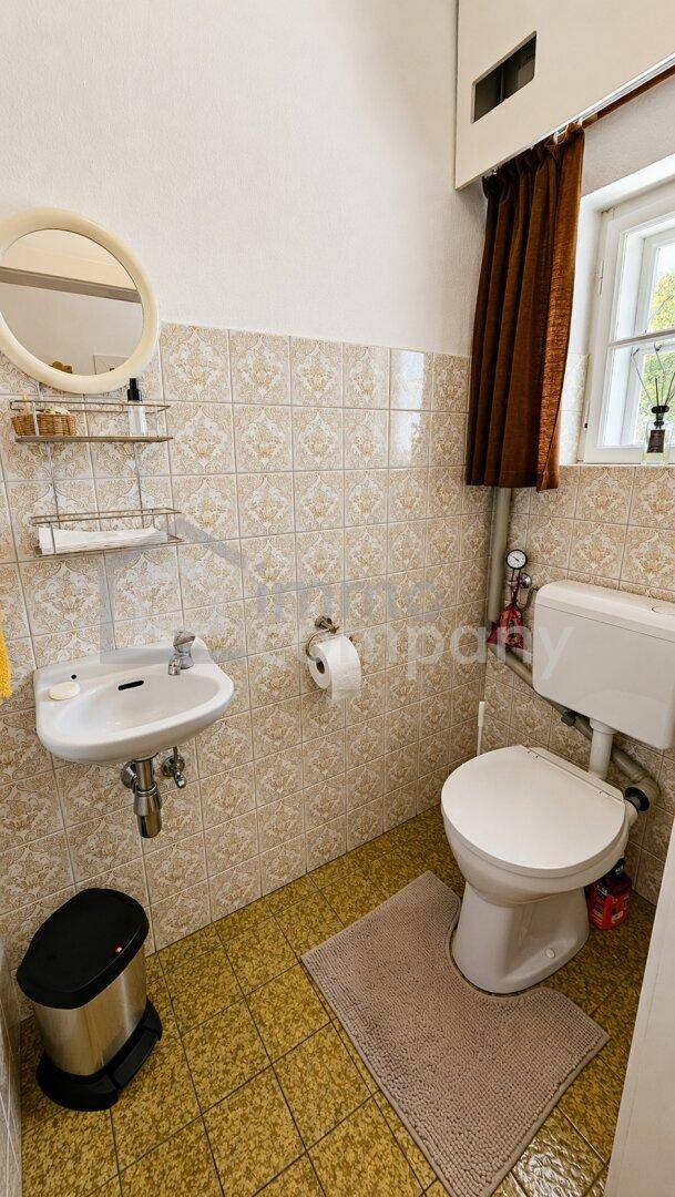 Gäste-WC mit Fliesenboden, Wand-WC und kleinem Waschbecken.