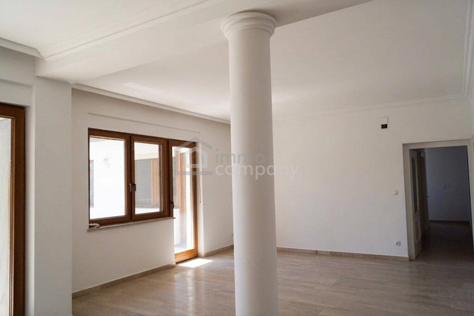 Helles Zimmer mit dekorativer Säule, Fliesenboden und Zugang zu einem Außenbereich.
