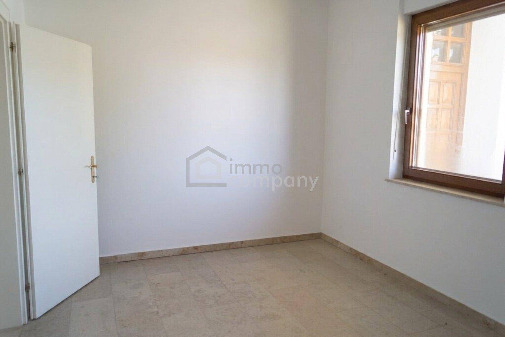 Helles Zimmer mit Fliesenboden, weißer Tür und einem Fenster.