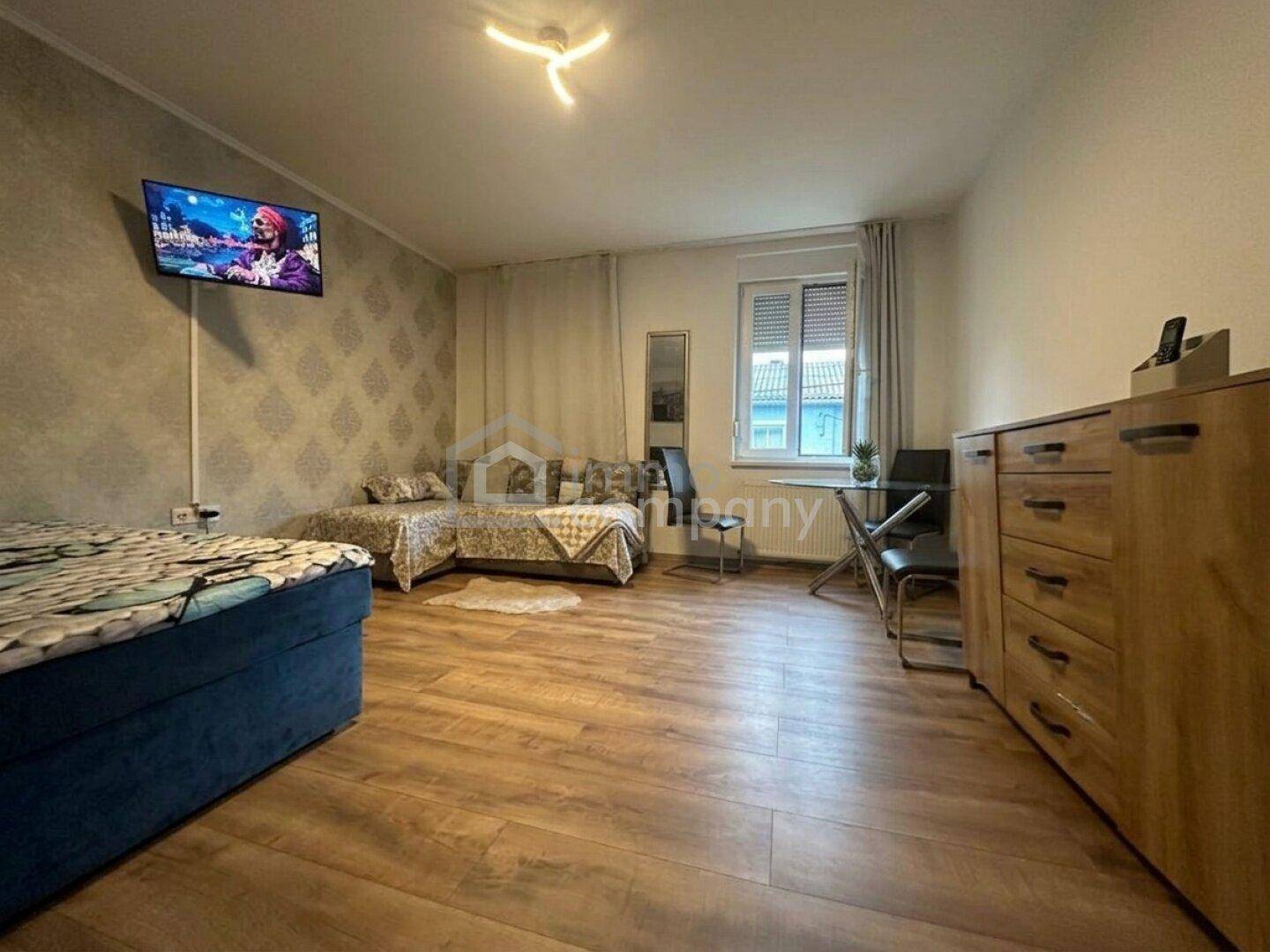 Heller Wohnbereich mit Laminatboden, bequemen Betten und einem Fenster mit Rollläden.