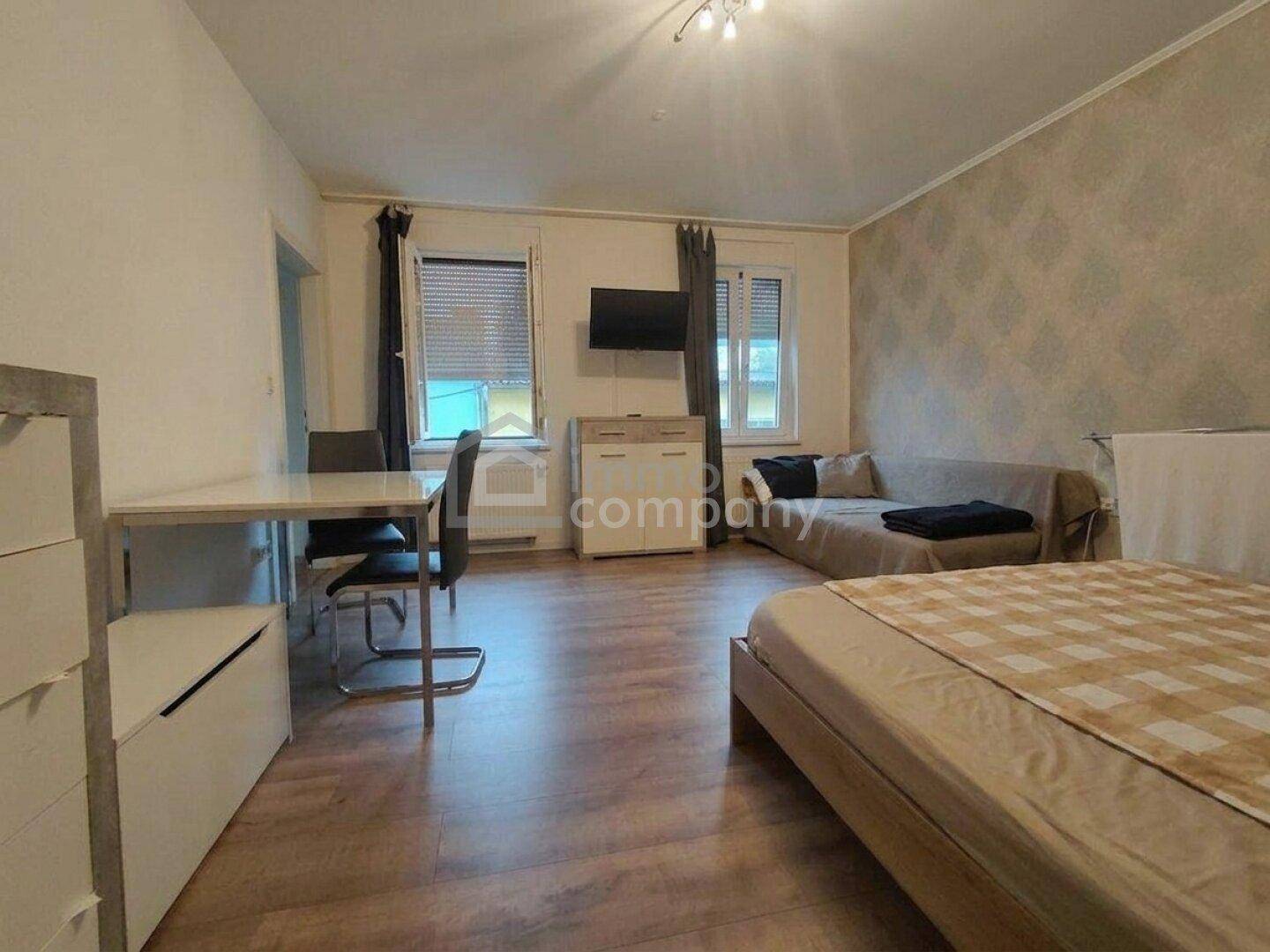 Funktionaler Wohn- und Schlafbereich mit Laminatboden, einem Bett und einem kleinen Esstisch.