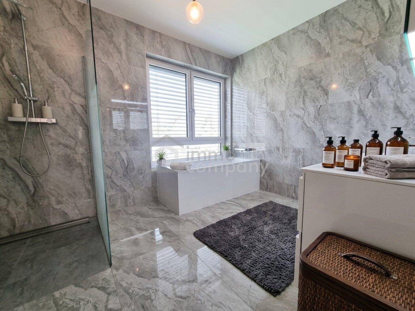 Modernes Badezimmer mit grauen Marmorfliesen, begehbarer Dusche und Badewanne am Fenster.