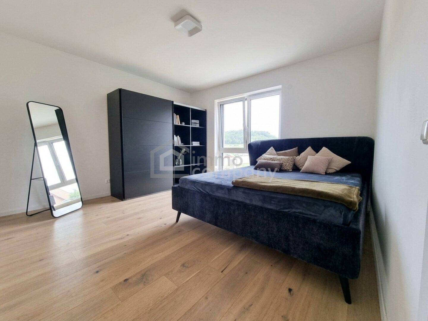 Schlafzimmer mit dunklem Bett, schwarzem Kleiderschrank und Holzfußboden, hell durch Fenster.