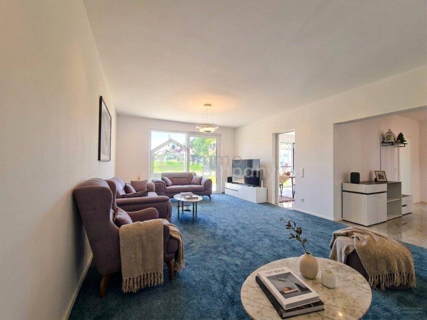 Gemütliches Wohnzimmer mit blauem Teppich, bequemen Sofas und hellem Fensterbereich.