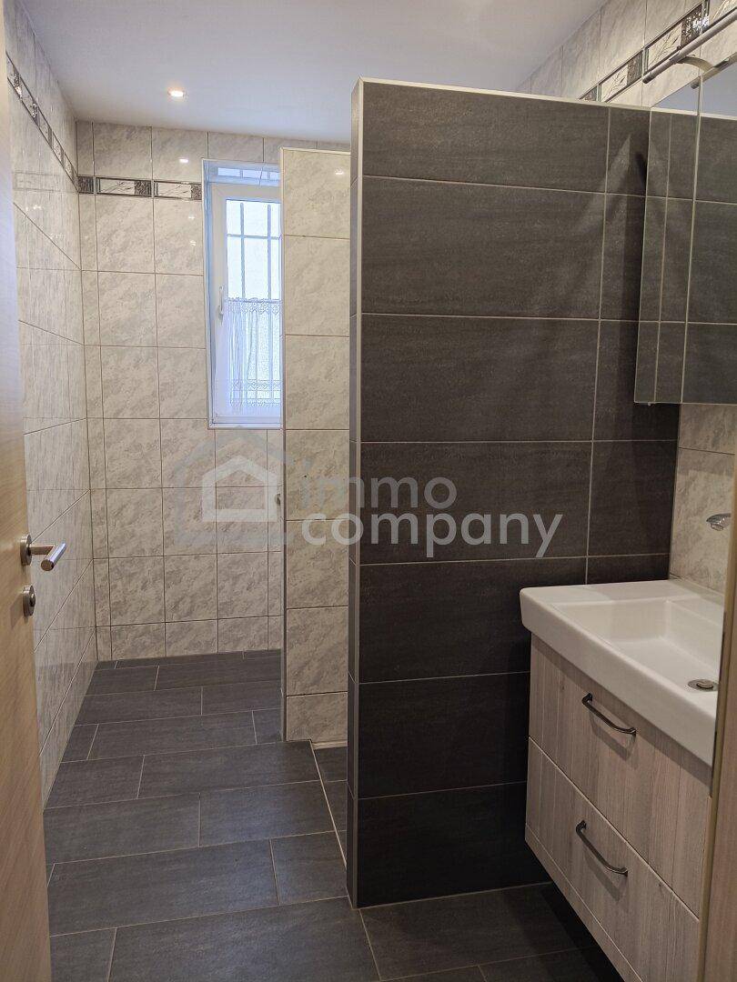 Modernes Badezimmer mit begehbarer Dusche, Einzelwaschbecken und Fliesen an Wänden und Boden.