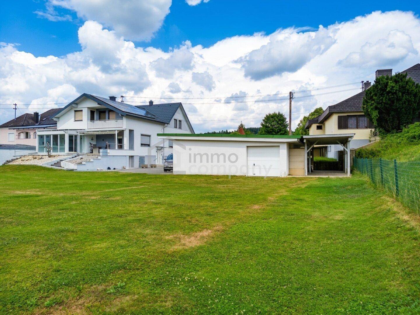 Ansicht des Hauses von der Seite mit großem Rasen, Garage und Carport im sonnigen Garten.