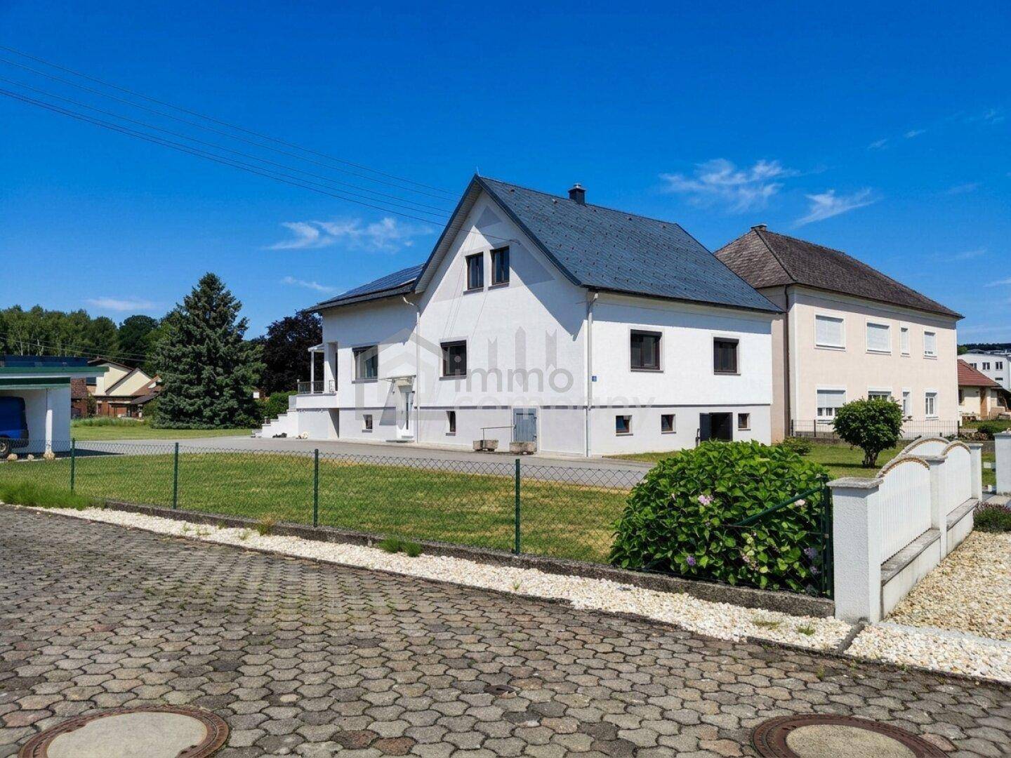 Seitenansicht des Hauses mit gepflasterter Auffahrt, kleinem Vorgarten und blauem Himmel.