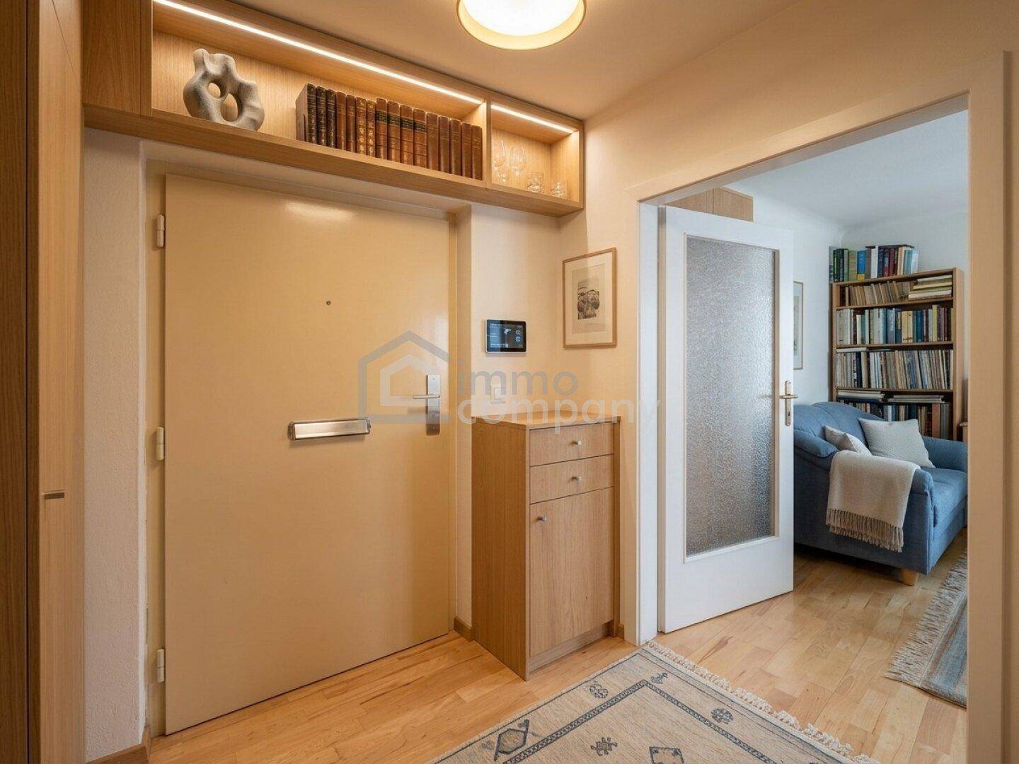 Heller Eingangsbereich mit Holzboden und Zugang zu einem gemütlichen Wohnzimmer mit Bücherregal.