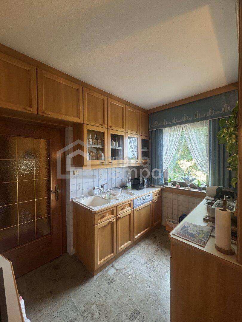Helle Küche mit Holzschränken, Spülbecken und Fenster mit Vorhängen, funktional eingerichtet.