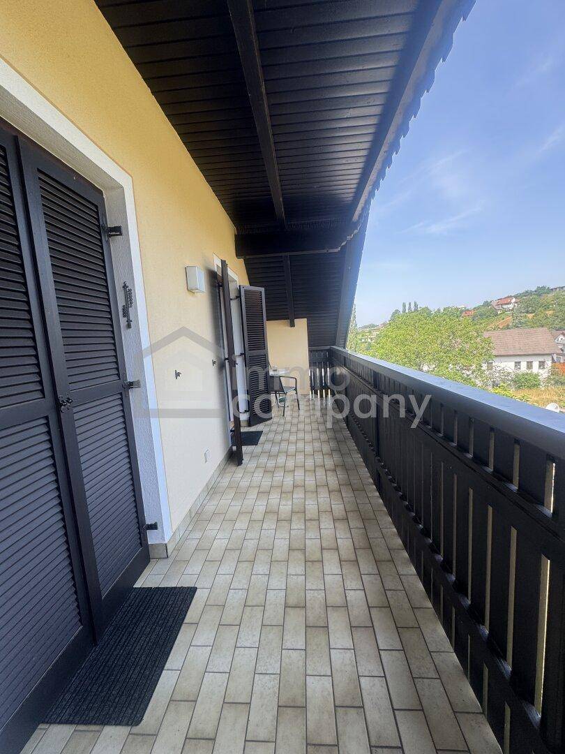 Langer Balkon mit Fliesenboden und dunklem Holzgeländer, bietet einen weiten Ausblick.