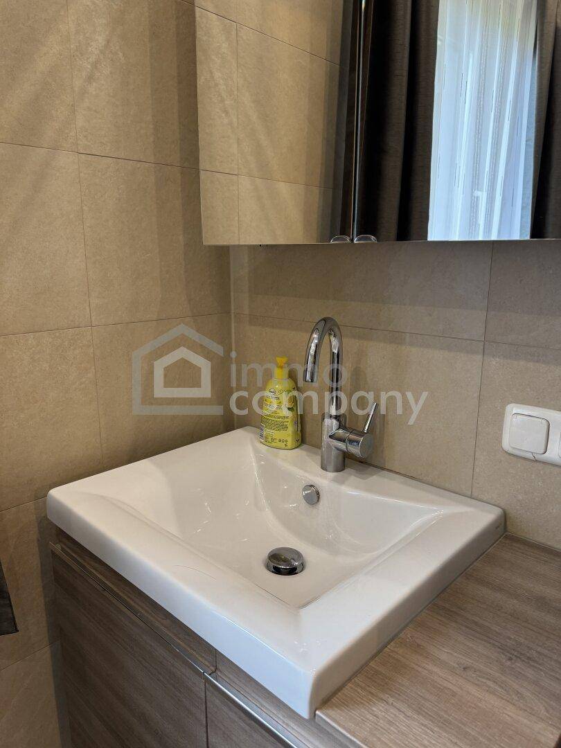 Modernes Badezimmer mit Einzelwaschbecken, Spiegelschrank und hellen Fliesen.