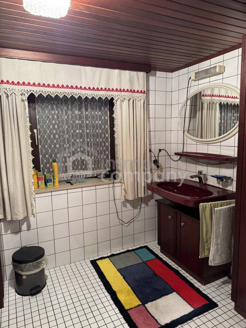 Badezimmer im 80er-Jahre-Stil mit roten Armaturen, Fliesen und Fenster mit Vorhängen.