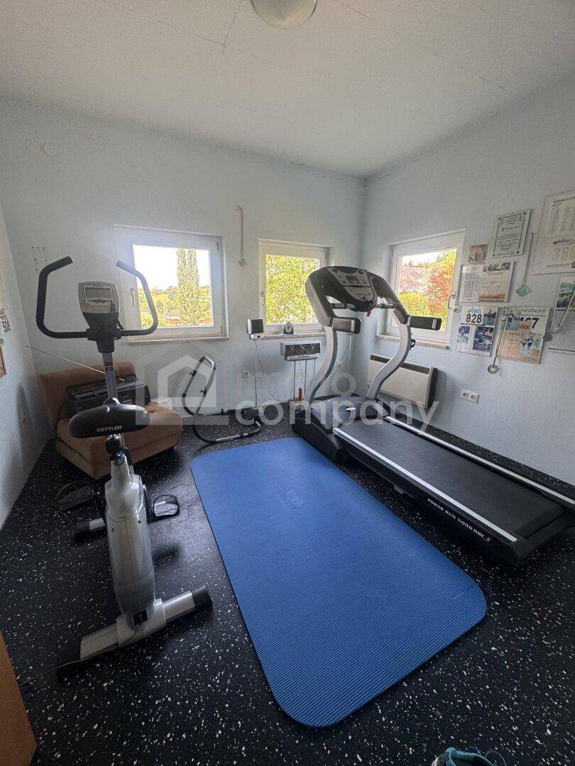 Fitnessraum mit Laufband, Heimtrainer und Fenstern, ideal für sportliche Aktivitäten.