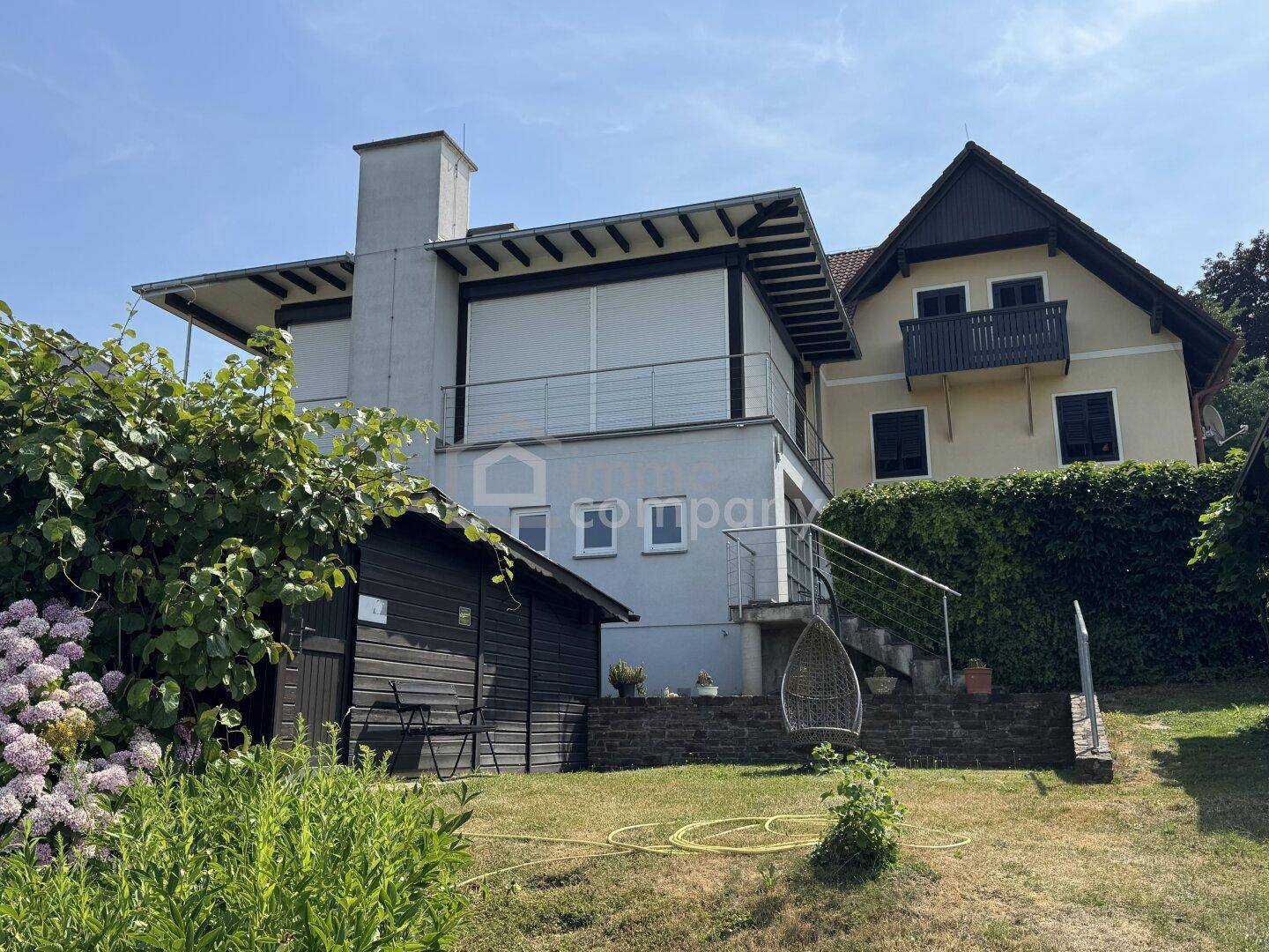 Gesamtansicht des Hauses mit Garten, Schuppen und einer Außentreppe unter blauem Himmel.
