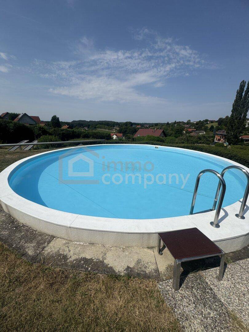 Runder Pool mit blauer Abdeckung und Einstiegsleiter im sonnigen Gartenbereich.