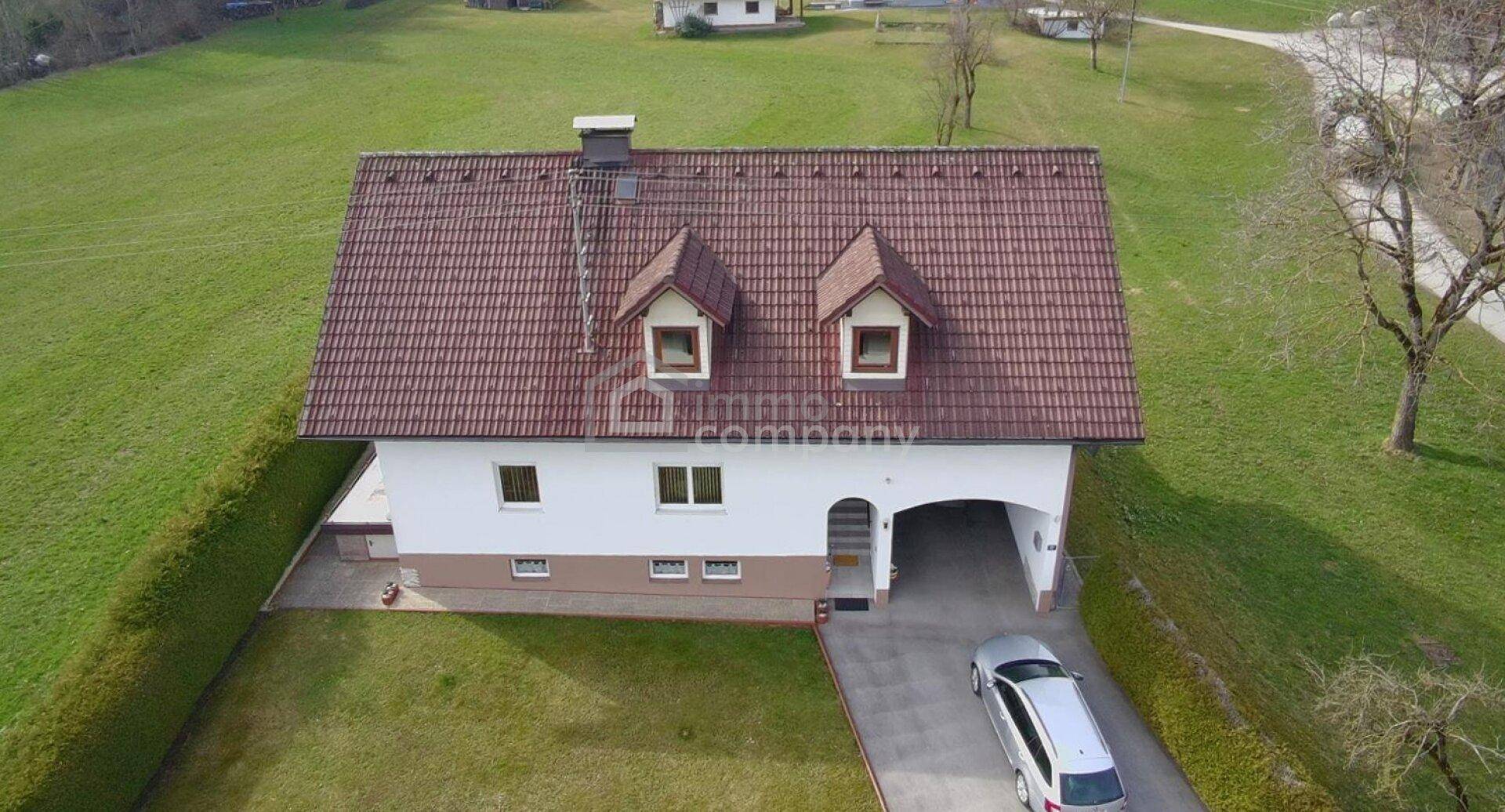 Luftaufnahme eines Einfamilienhauses mit rotem Ziegeldach, Gauben und integriertem Carport.