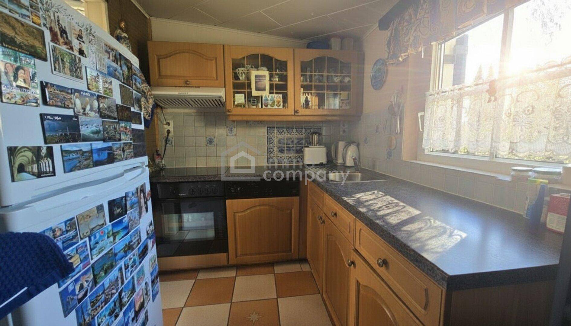 Gemütliche Küche mit Holzschränken, Fliesenboden und viel Tageslicht durch das Fenster.