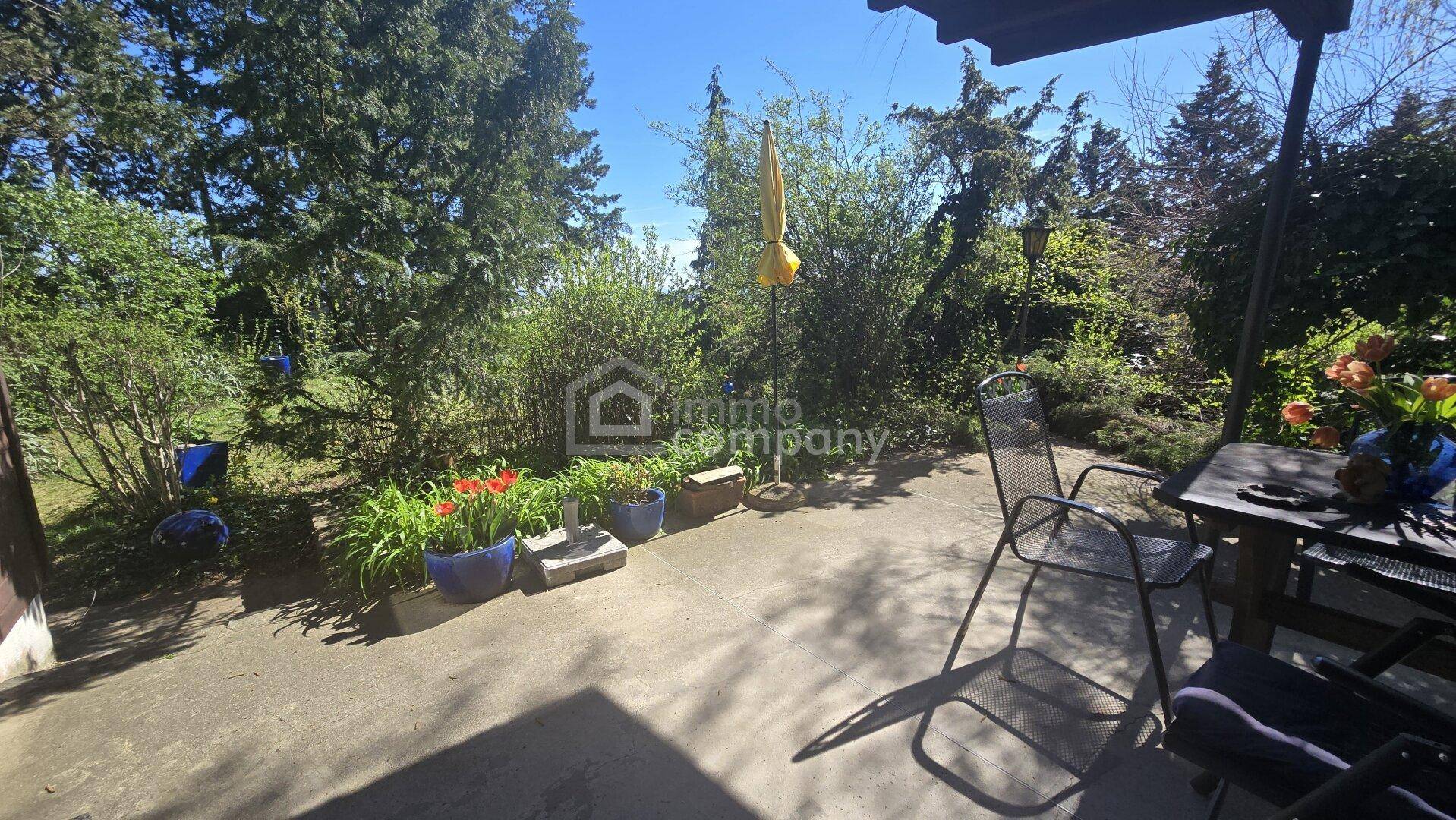 Sonnige Terrasse mit Gartenmöbeln und üppiger Bepflanzung, ideal zum Entspannen im Freien.