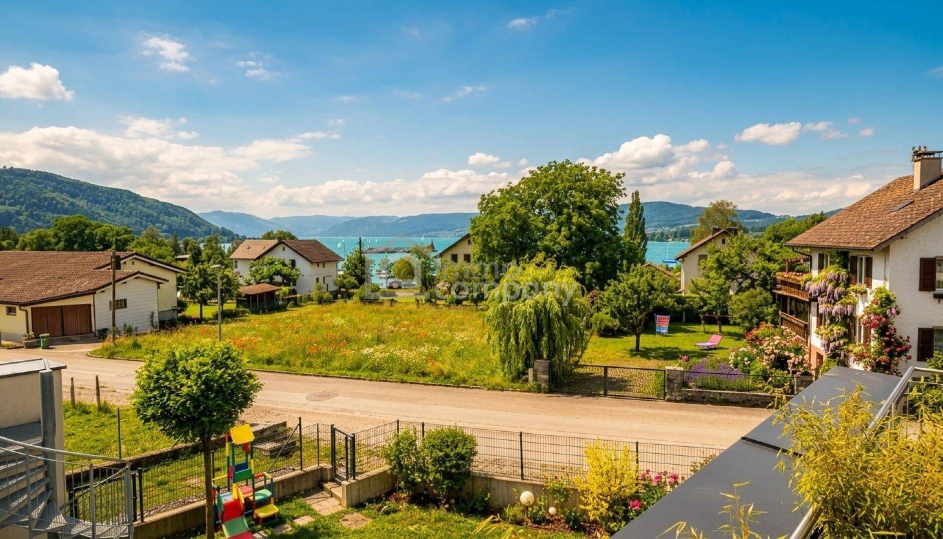 Panoramablick auf den See und die umliegenden Berge mit grüner Landschaft und Häusern.