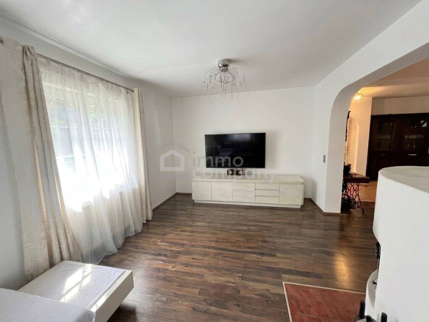 Helles Wohnzimmer mit großem Fenster, Holzboden und einem modernen TV-Möbel.