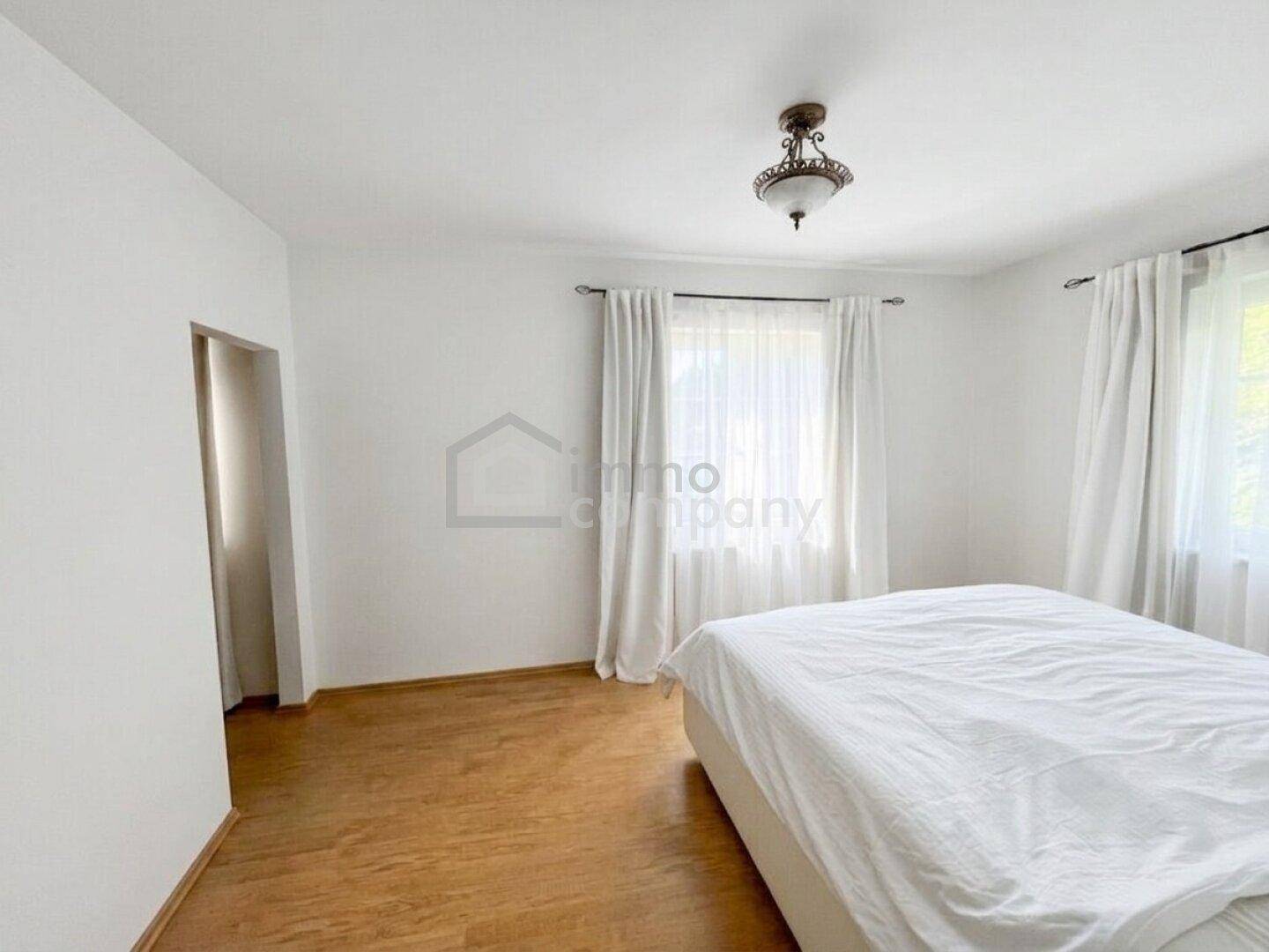 Schlafzimmer mit hellem Holzboden, weißen Wänden und einem großen Fenster für viel Tageslicht.