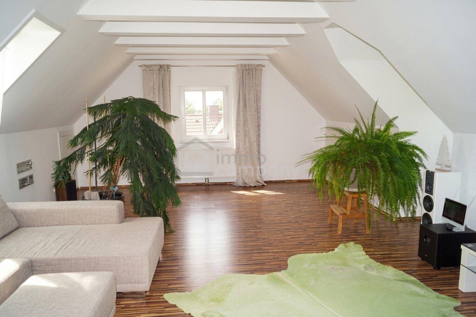 Geräumiges Dachzimmer mit schrägen Decken, Holzboden und großen Pflanzen als Dekoration.
