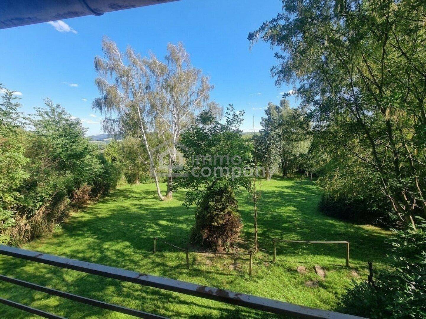 Panoramablick von einem Balkon auf einen weitläufigen, grünen Garten mit verschiedenen Bäumen und Sträuchern.