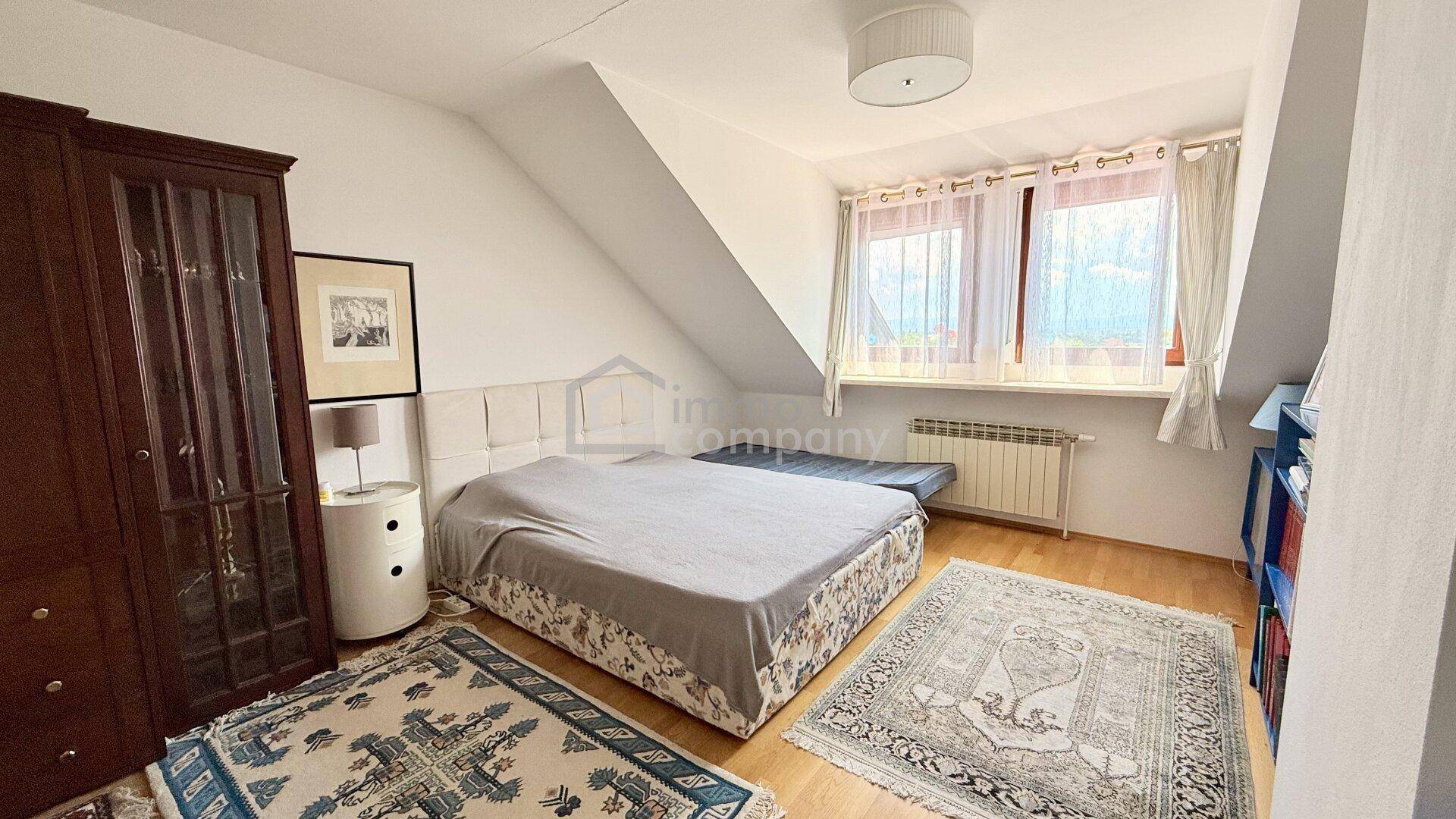 Schlafzimmer mit Doppelbett, Kleiderschrank und Fenster unter einer Dachschräge.