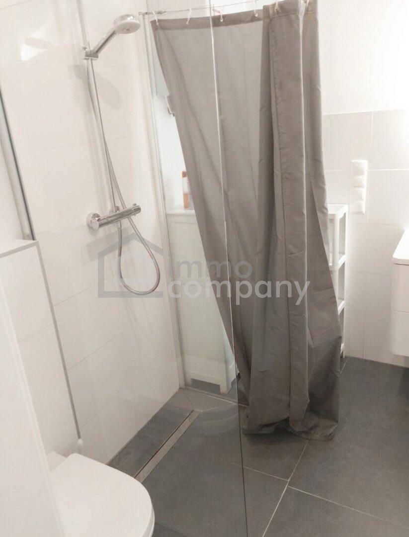 Modernes Badezimmer mit ebenerdiger Dusche, Glasabtrennung und grauen Bodenfliesen.