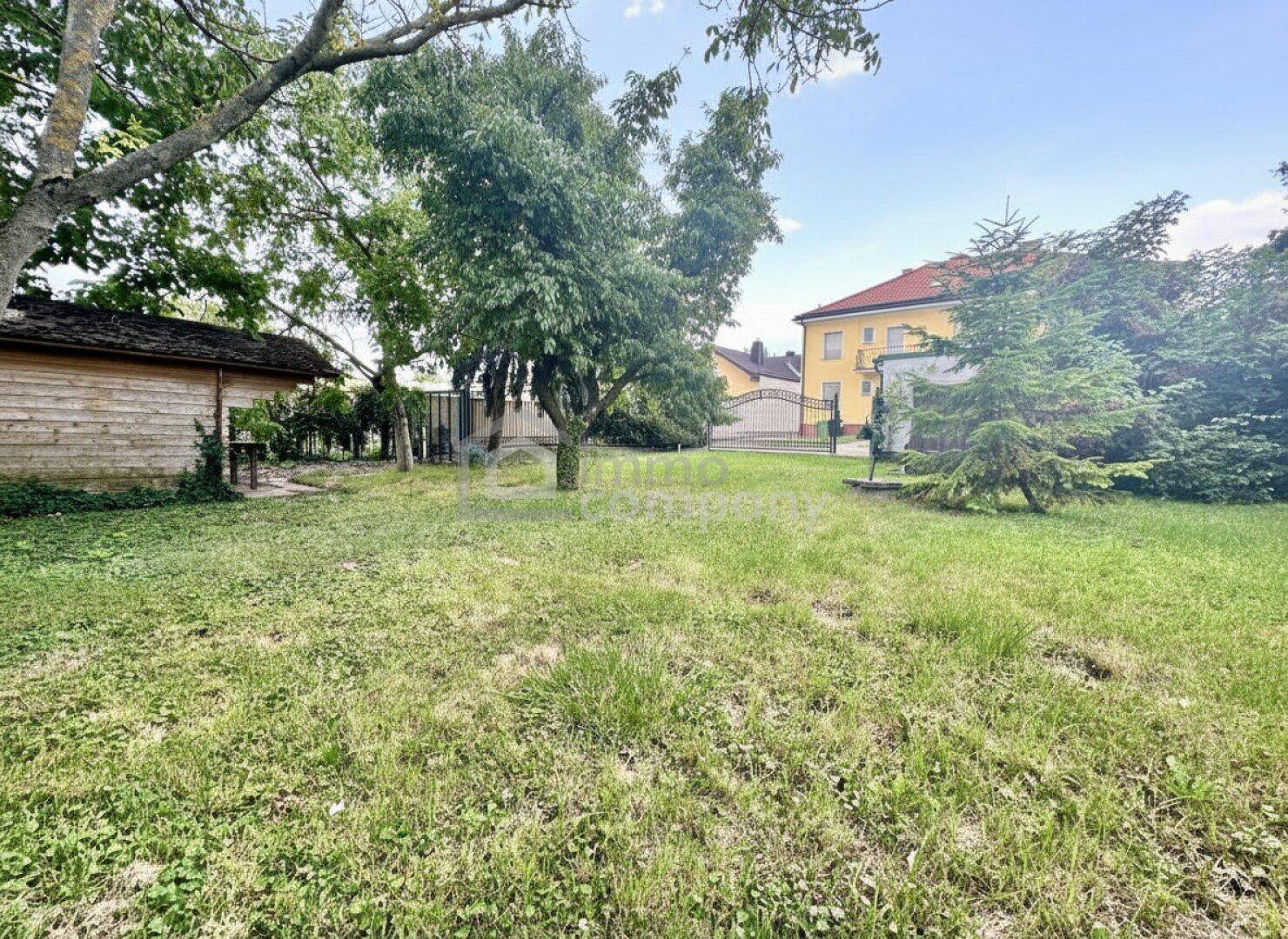 Großer Gartenbereich mit Rasenfläche, Bäumen und einem Gartenhaus im Hintergrund.