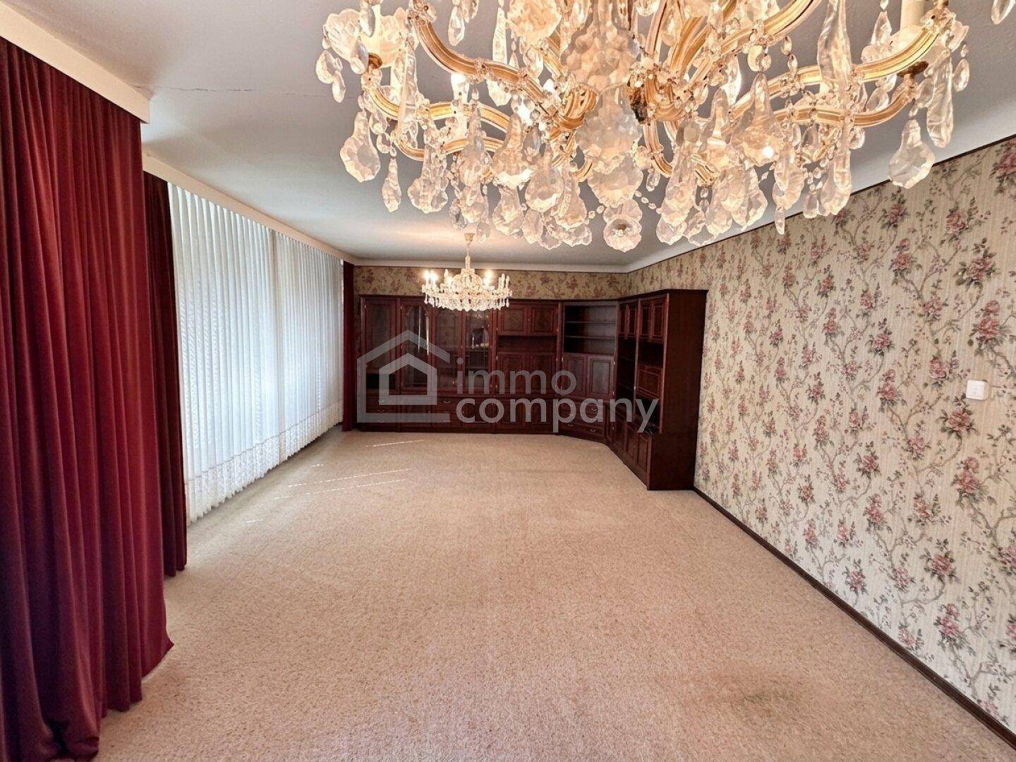 Geräumiges Wohnzimmer mit floraler Tapete, Teppichboden und opulentem Kronleuchter.