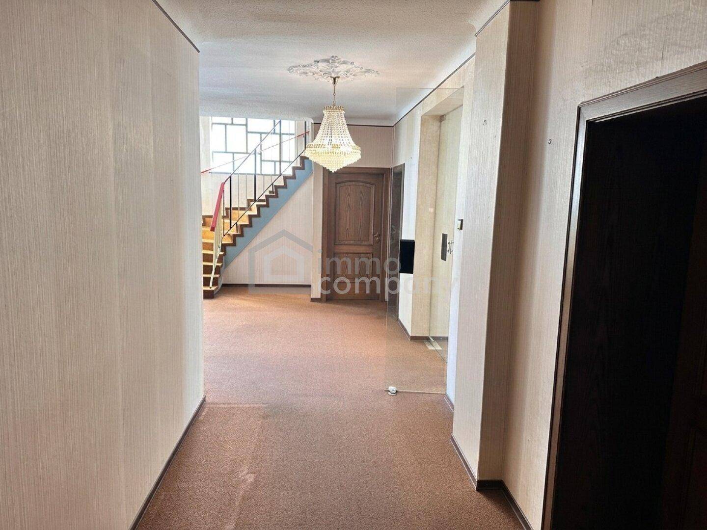 Geräumiger Flur mit Teppichboden, Treppe zum Obergeschoss und elegantem Kronleuchter.