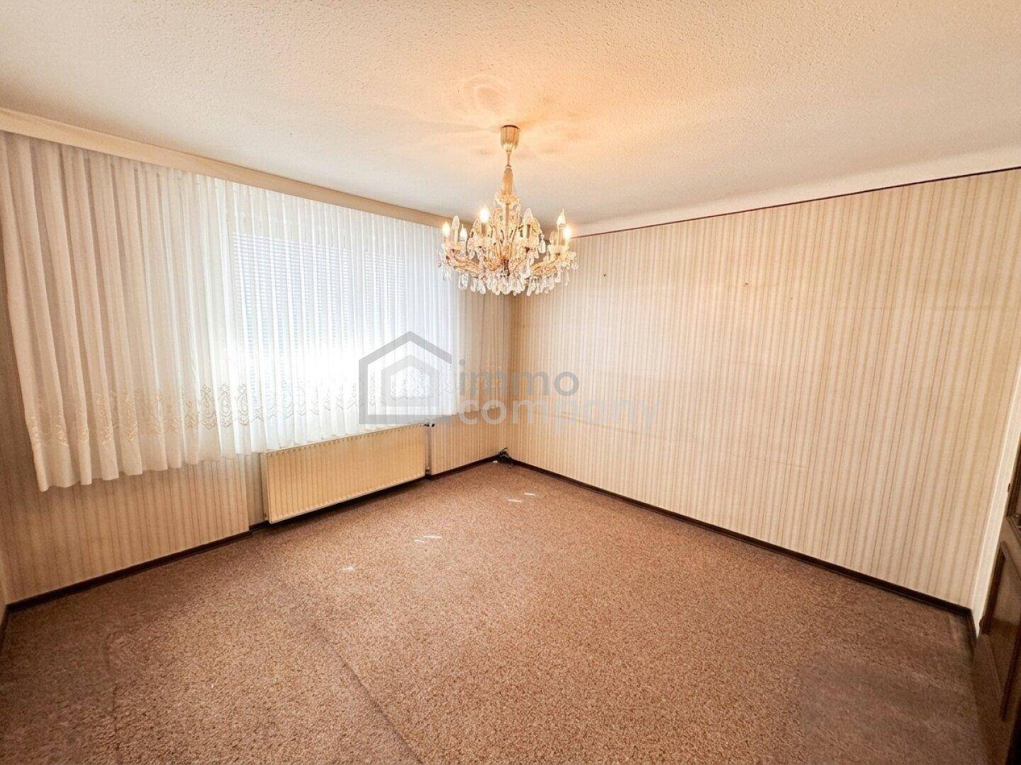 Schlafzimmer mit Teppichboden, gemusterter Tapete und klassischem Kronleuchter.
