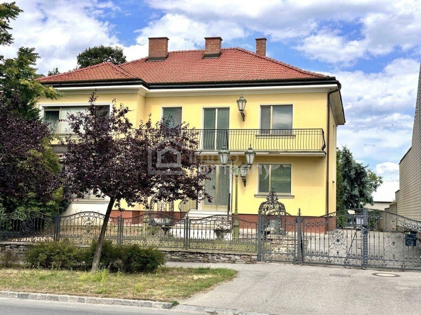 Klassische Villa mit gelber Fassade, Ziegeldach und dekorativem schmiedeeisernem Tor.