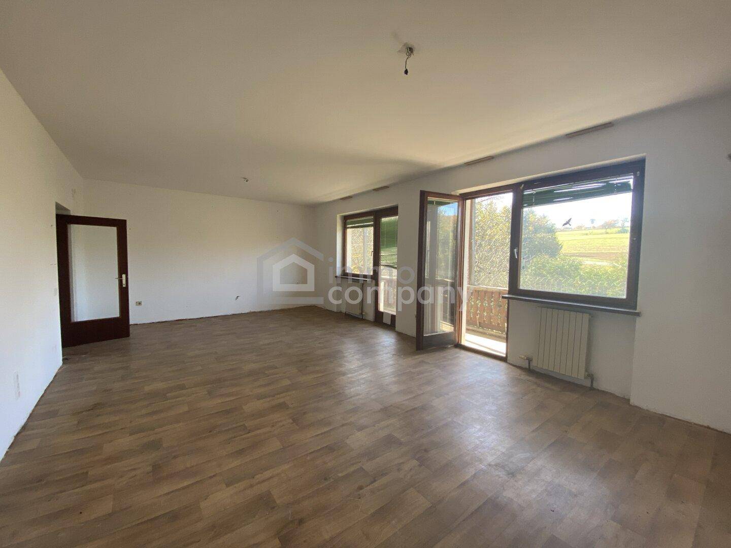 Helles, leeres Zimmer mit Holzboden und Zugang zu einem Balkon, bereit zur individuellen Gestaltung.