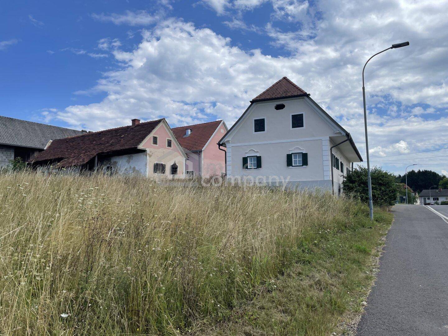Traditionelles Haus neben einem Feld und einer Straße, umgeben von ländlicher Landschaft.