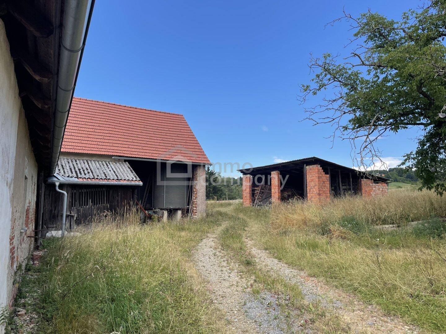 Ländliche Szene mit alten Scheunen und einem Feldweg unter strahlend blauem Himmel.