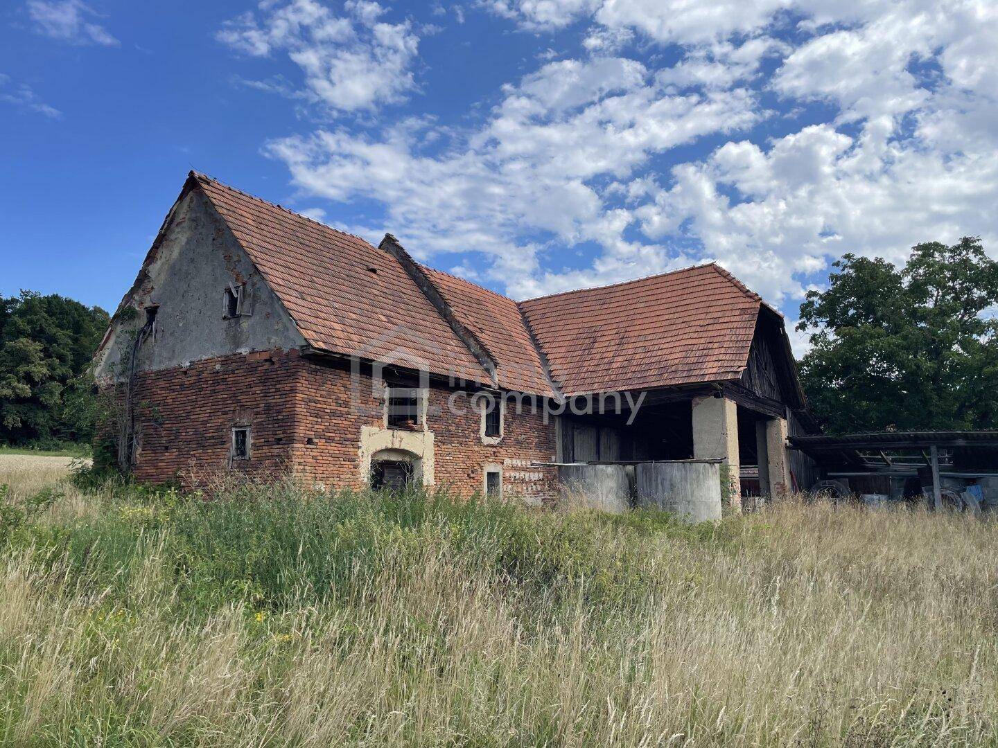 Großes, altes Backsteingebäude mit Ziegeldach und verwitterter Fassade auf einem Feld.