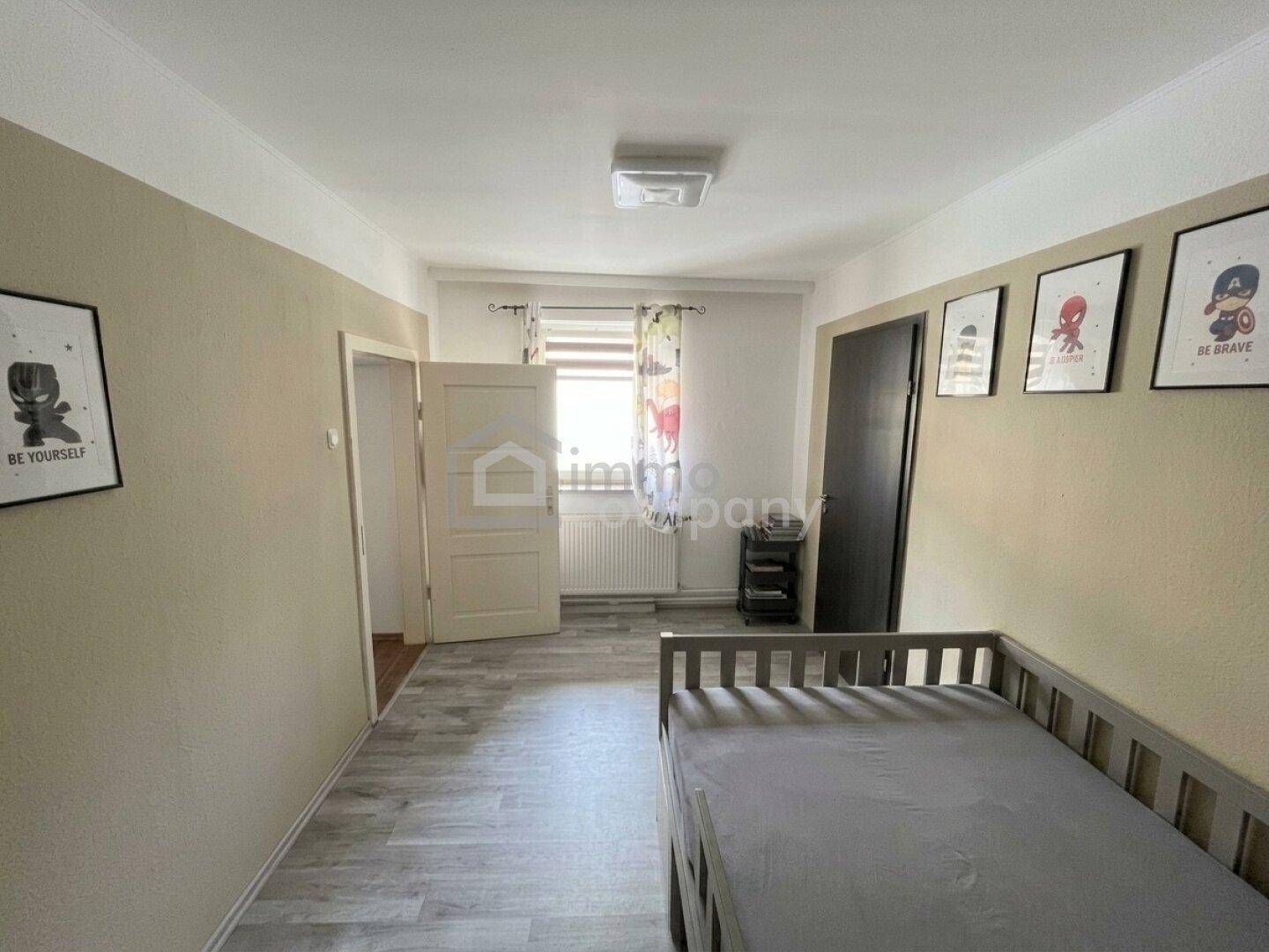 Kinderzimmer mit Gitterbett, hellen Wänden und bunten Bildern an der Wand.