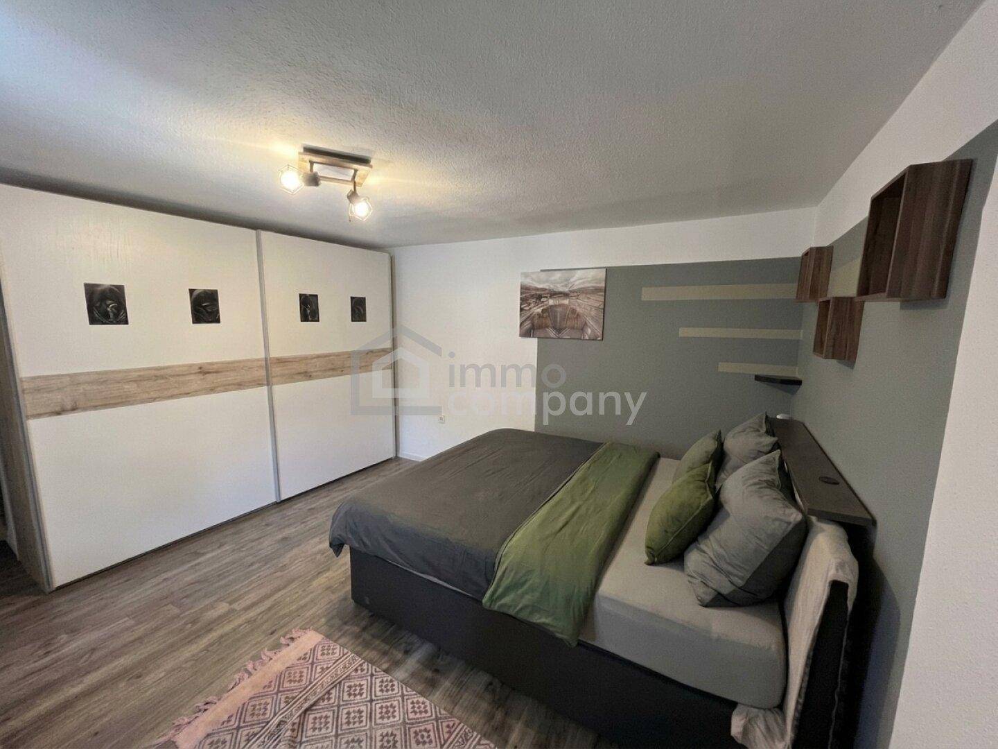 Schlafzimmer mit großem Bett, Einbauschränken und moderner Wandgestaltung in Grau und Weiß.