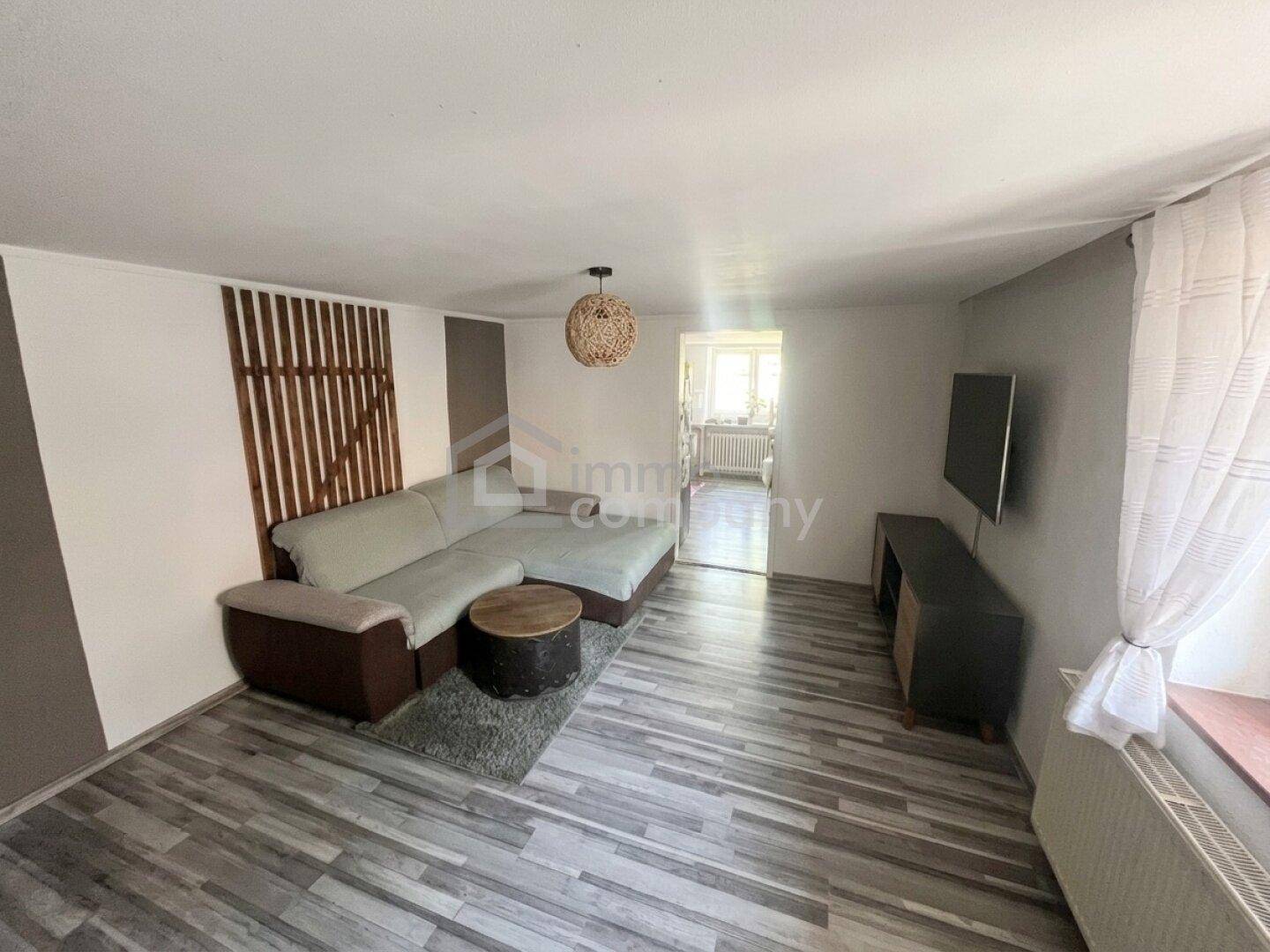 Gemütliches Wohnzimmer mit Ecksofa, Holzelementen und einem Fernseher an der Wand.