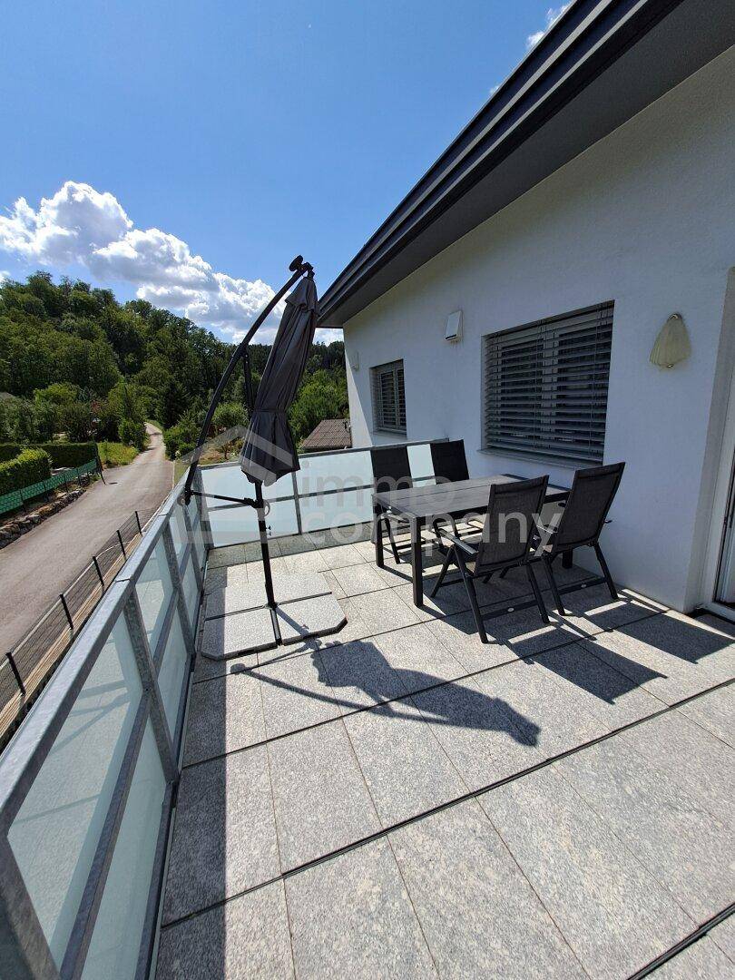 Sonniger Balkon mit Fliesenboden, Gartenmöbeln und Blick ins Grüne.