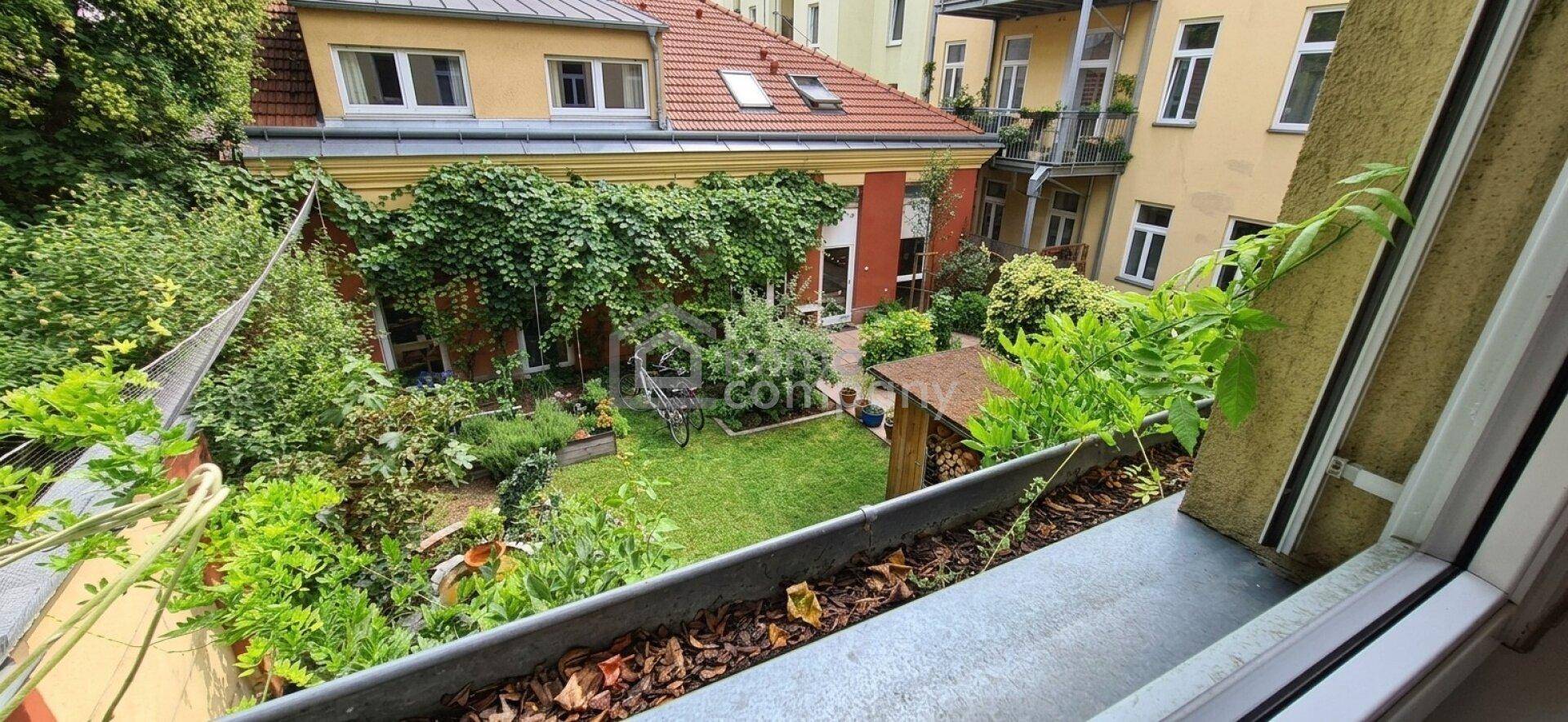 Blick von oben auf einen gepflegten Garten mit Rasenfläche und üppiger Bepflanzung zwischen Gebäuden.
